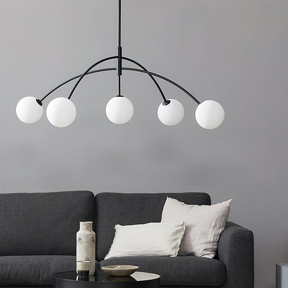 Black and white Clérachic chandelier with five globes on arched arms, hung above a charcoal sofa with linen cushions.