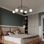 Black and white Clérachic chandelier lit in a bedroom with deep green walls, a tan leather bed and white fitted wardrobes.
