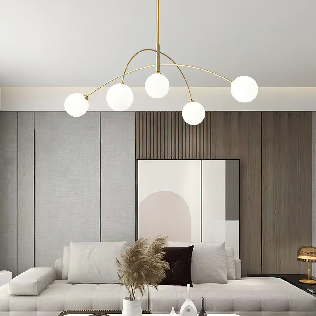 Gold and white Clérachic chandelier over a cream sofa with pampas grass in a vase, in front of a wood-slat wall.
