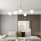 Gold and white Clérachic chandelier over a cream sofa with pampas grass in a vase, in front of a wood-slat wall.