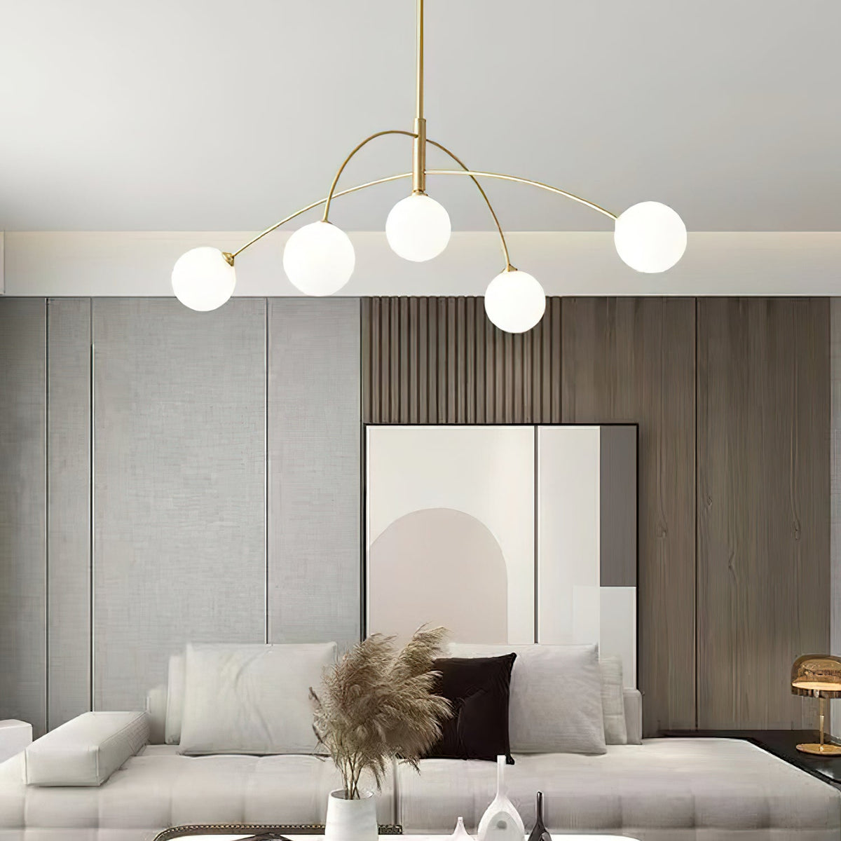 Gold and white Clérachic chandelier over a cream sofa with pampas grass in a vase, in front of a wood-slat wall.