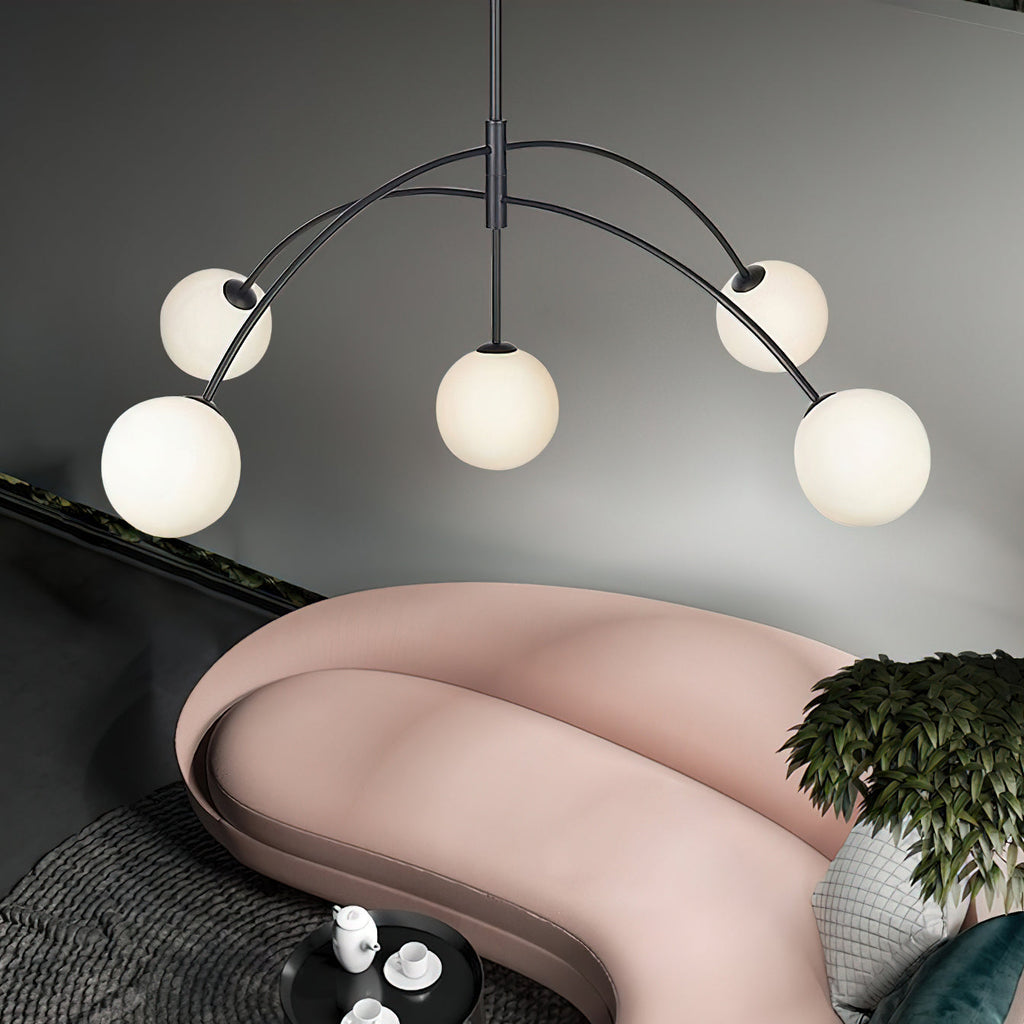 Black and white Clérachic chandelier seen up close, its arms sweeping out over a curved pink sofa with a potted plant.
