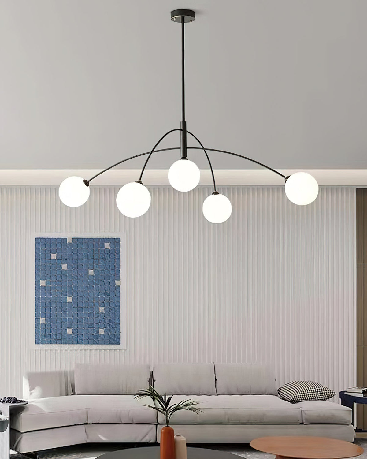 Black and white Clérachic chandelier over a pale sofa, a tall ribbed wall and a blue mosaic print behind.