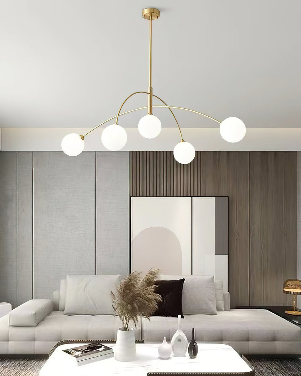 Gold and white Clérachic chandelier with a slim brass rod, hung low above a white coffee table and a sofa.