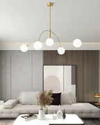 Gold and white Clérachic chandelier with a slim brass rod, hung low above a white coffee table and a sofa.