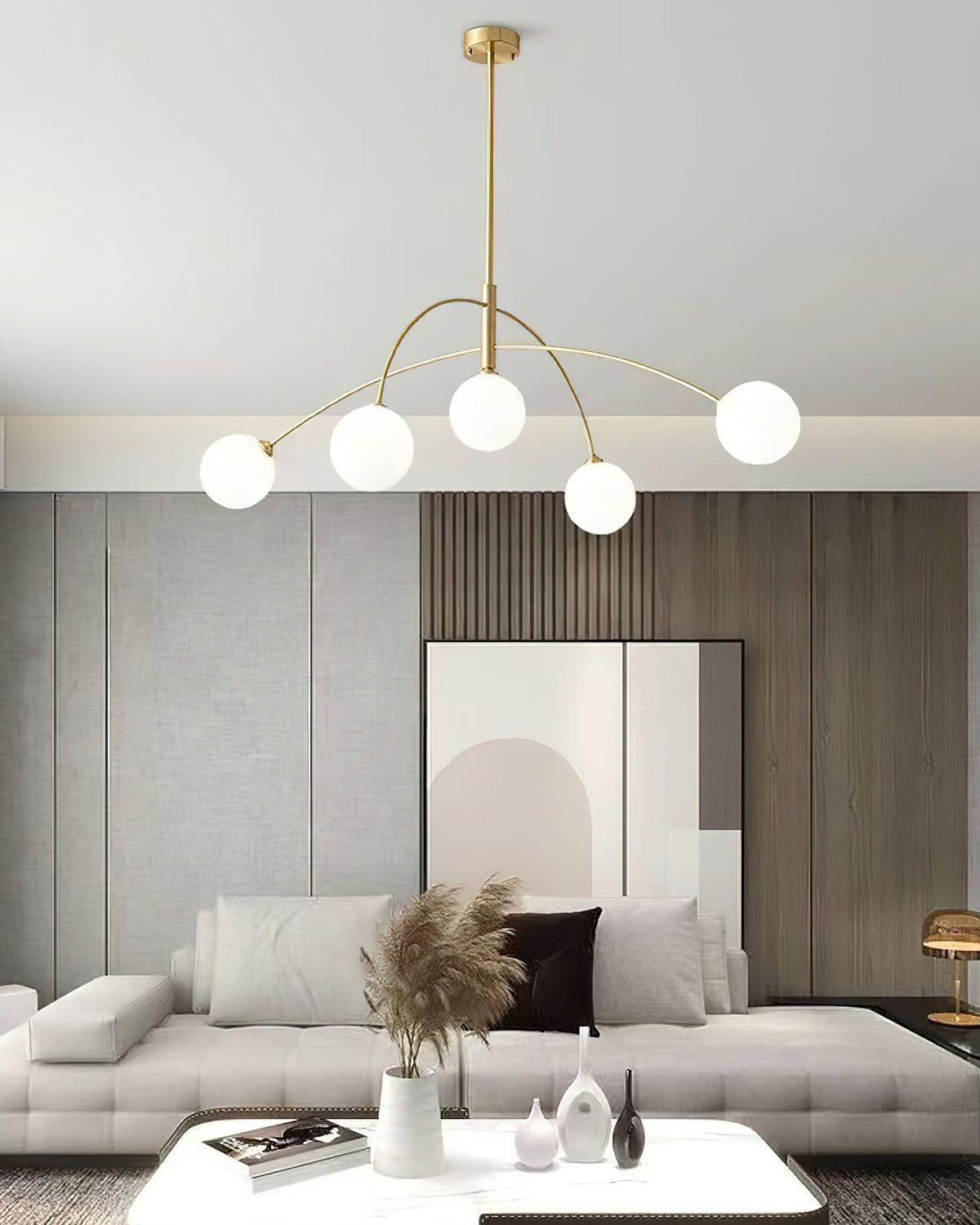 Gold and white Clérachic chandelier with a slim brass rod, hung low above a white coffee table and a sofa.