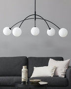 Black and white Clérachic chandelier with five frosted globes, hanging in front of a grey wall above a dark sofa.