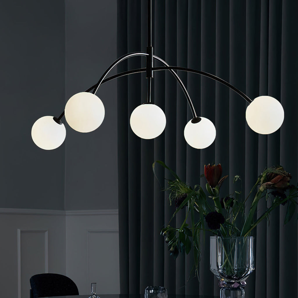 Black and white Clérachic chandelier against a dark curtain, its globes lit and a vase of flowers on the table below.