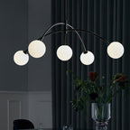 Black and white Clérachic chandelier against a dark curtain, its globes lit and a vase of flowers on the table below.