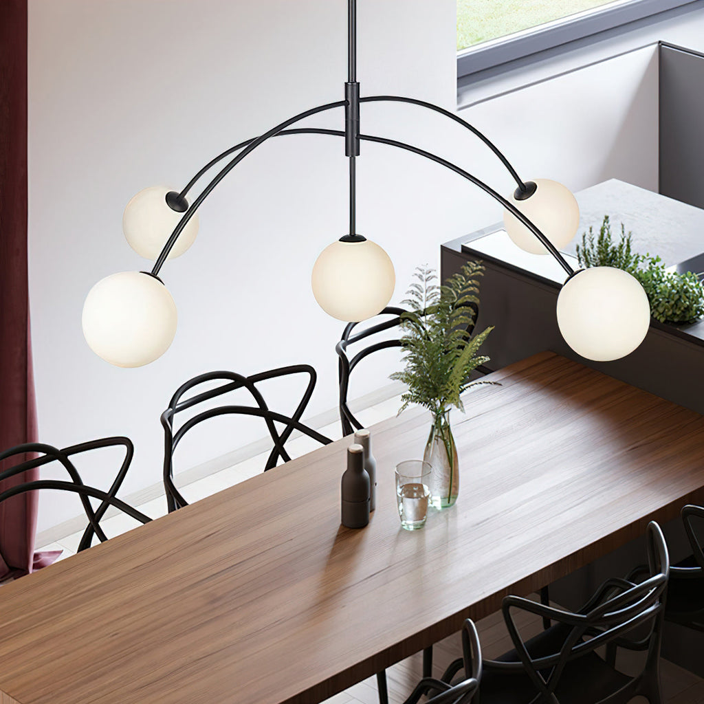Black and white Clérachic chandelier seen from above a dark wood dining table with woven black chairs and a glass vase of ferns.