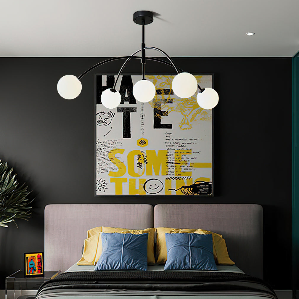 Black and white Clérachic chandelier in a dark bedroom, above a grey bed with blue and mustard cushions and a graphic poster.