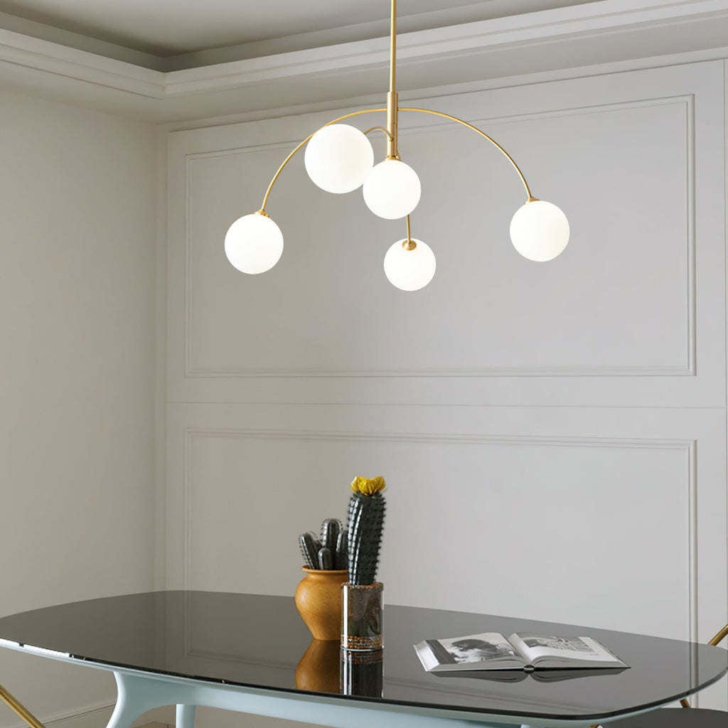 Gold and white Clérachic chandelier in a panelled room, five lit globes over a glass table with a cactus and a book.
