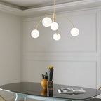 Gold and white Clérachic chandelier in a panelled room, five lit globes over a glass table with a cactus and a book.