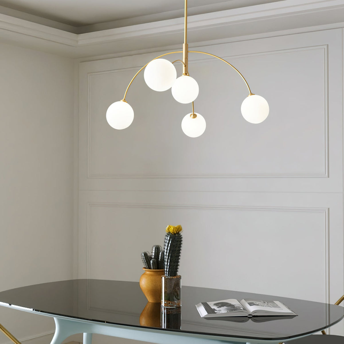 Gold and white Clérachic chandelier in a panelled room, five lit globes over a glass table with a cactus and a book.