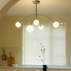 Clérachic chandelier with a pewter-grey rod and arms and five lit globes, hung in front of a window with blinds in a warm-toned room.