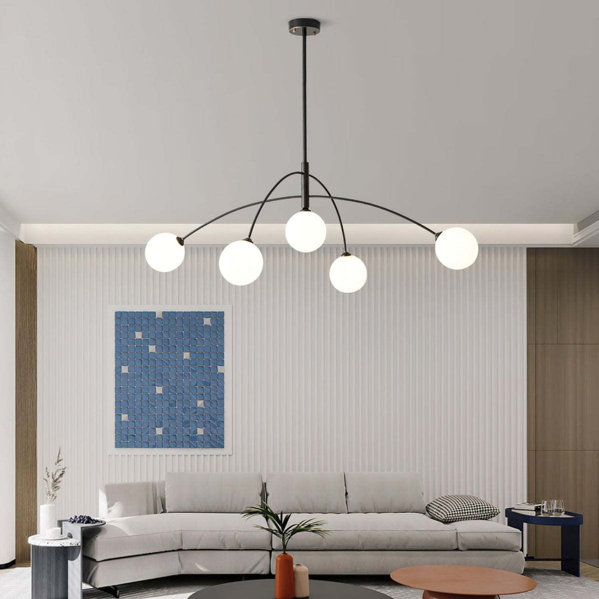 Black and white Clérachic chandelier lit in front of a ribbed wall with a blue mosaic print, above a pale sofa.