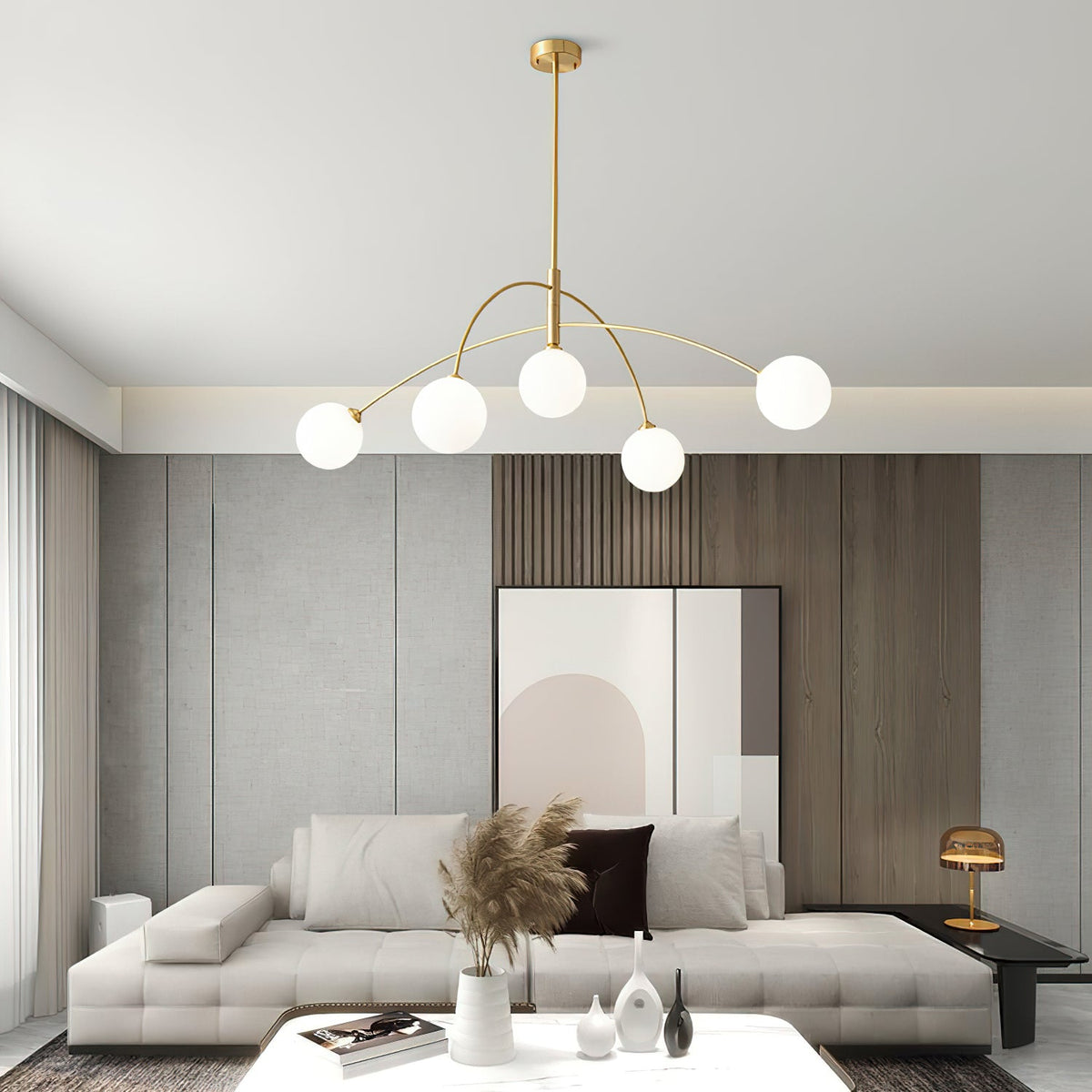 Gold and white Clérachic chandelier in a grey living room, with a large pale print and pampas grass on a coffee table.