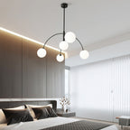 Black and white Clérachic chandelier above a dark-toned bed with black and cream cushions, a recessed ceiling light strip above.