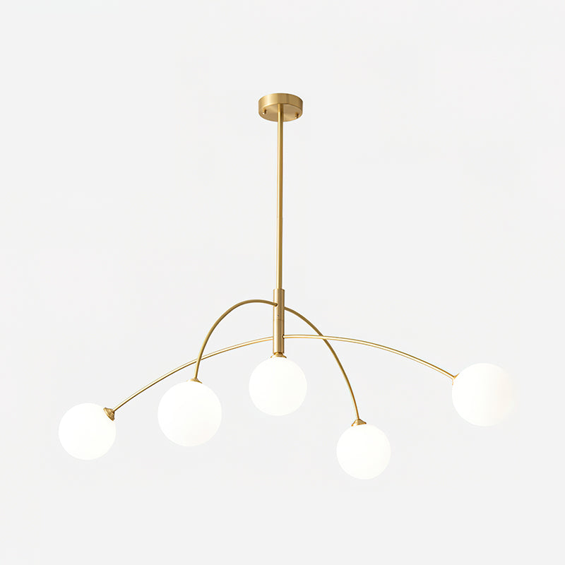 Gold and white Clérachic chandelier lit against a soft grey backdrop, its globes glowing on thin brass arms.