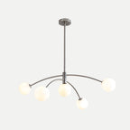 Chrome Clérachic chandelier with lit globes, a round ceiling plate and a slim rod on a pale background.