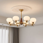 Under a carved plaster ceiling rose, a Clérachic chandelier with milky globes and brass arms hangs beside grey and white curtains.