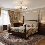 A Clérachic chandelier hangs above a dark four-poster bed with floral bedding, in a bedroom with cream panelled walls and a patterned rug.
