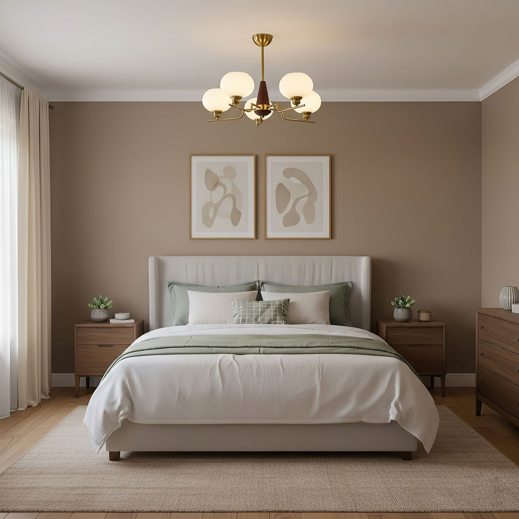 Five frosted globes on this Clérachic chandelier hang above a white bed with green cushions, in a bedroom with taupe walls.