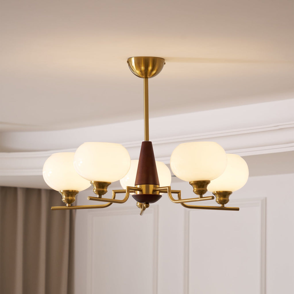 Seen from below, the white globes, brass arms and walnut centre cone of this Clérachic chandelier sit against a panelled wall.