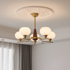 The milky globes of this Clérachic chandelier glow beneath an ornate plaster ceiling rose, beside curtains at the window.