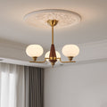 A three-light Clérachic chandelier with a brass rod and walnut cone hangs below a plaster ceiling rose, beside soft curtains.