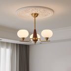 A three-light Clérachic chandelier with a brass rod and walnut cone hangs below a plaster ceiling rose, beside soft curtains.