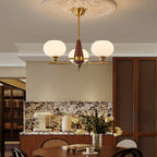 A Clérachic chandelier with three globes hangs over a dining area with round cane-back chairs and a marble splashback.