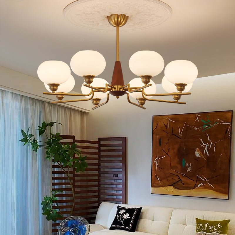 A Clérachic chandelier with eight globes hangs low in a bright living room, with a large painting and a cream sofa underneath.