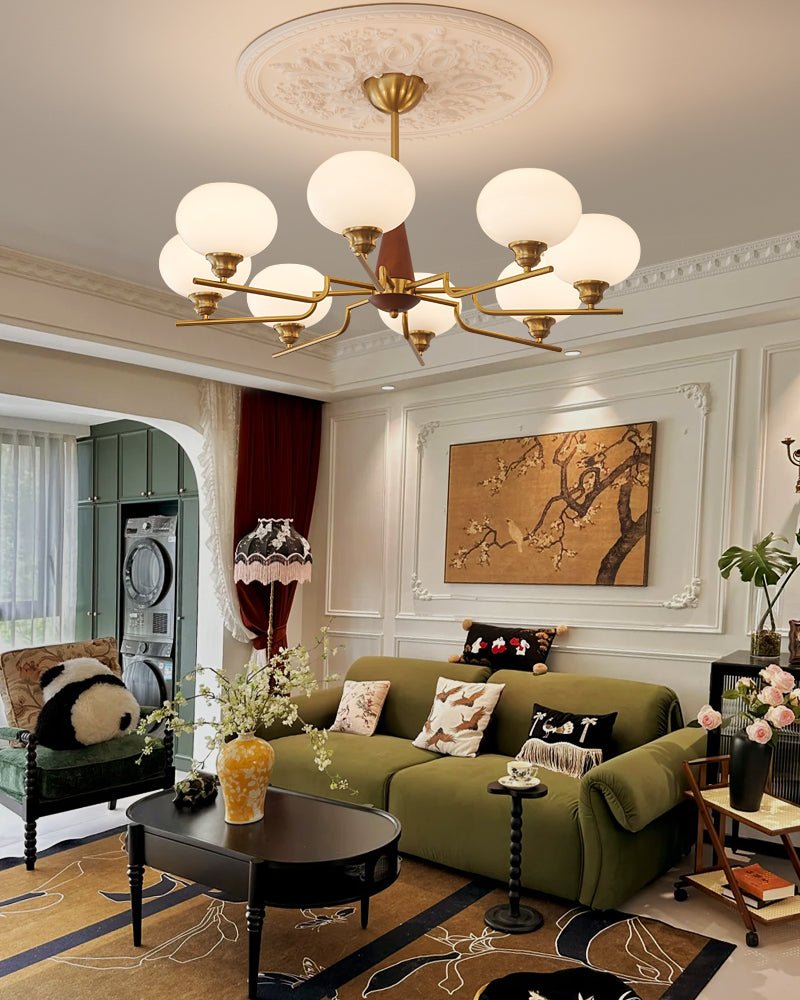 This Clérachic chandelier hangs in a living room with ornate wall mouldings, a green sofa and a patterned rug below.