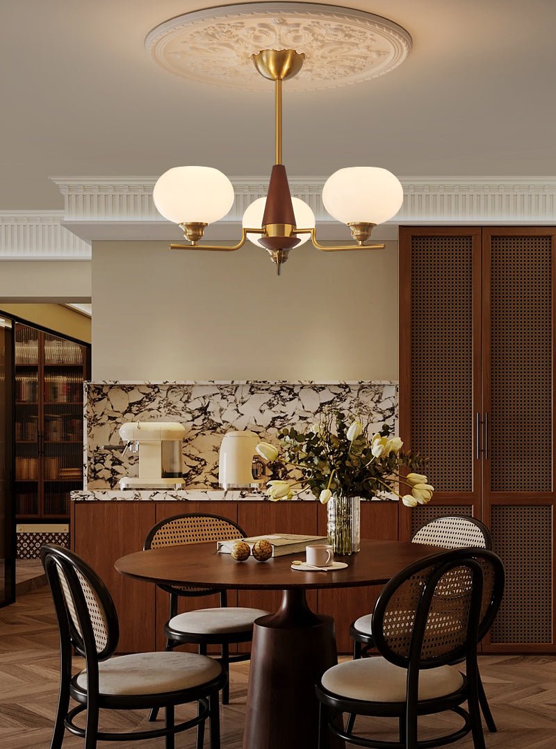 Over a dining table with black cane chairs, a three-light Clérachic chandelier hangs from a plaster ceiling rose.