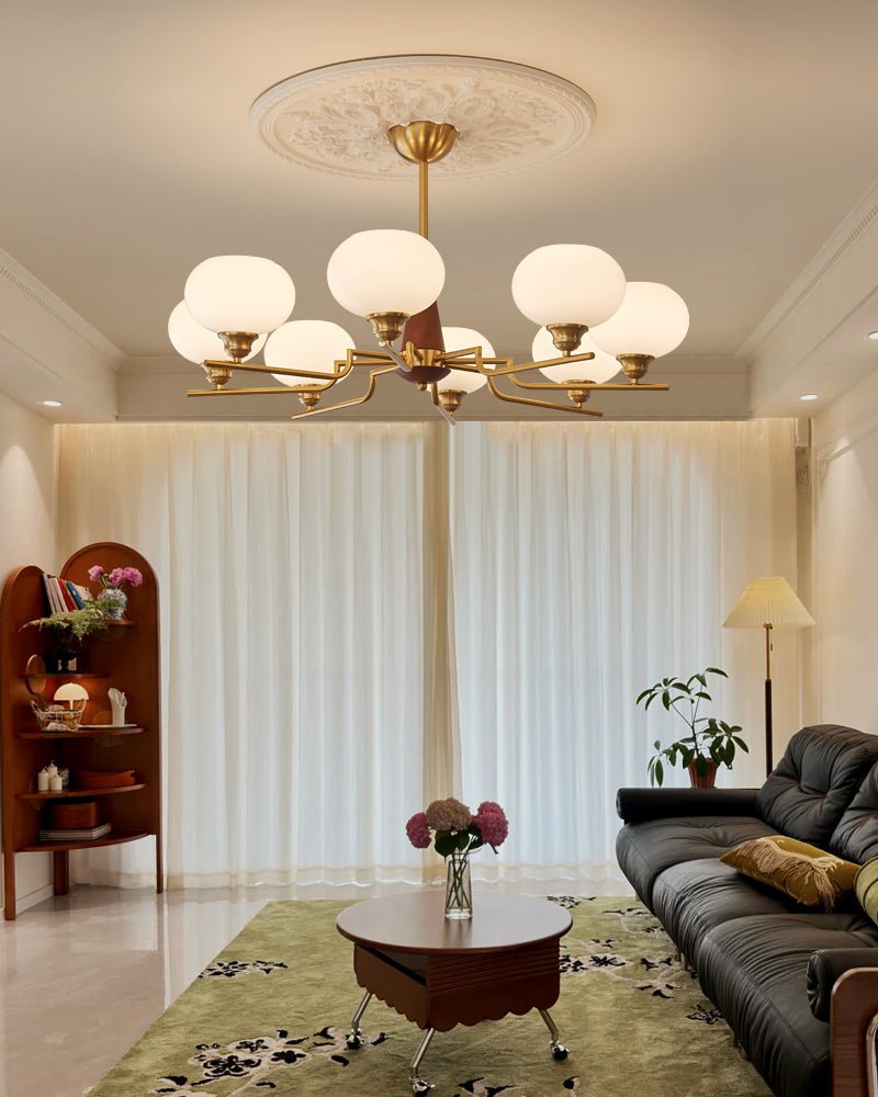 In a tall room with floor-length curtains, a Clérachic chandelier with eight globes hangs below a decorative ceiling rose.