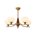 The brass canopy and rod of this Clérachic chandelier lead down to a walnut cone and three lit white globes, on white.