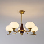 A lit Clérachic chandelier with five frosted globes hangs from a brass rod against a soft grey wall.