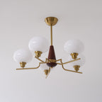 This Clérachic chandelier has white globes that look cooler and clearer, on brass arms and a walnut cone against a pale grey wall.