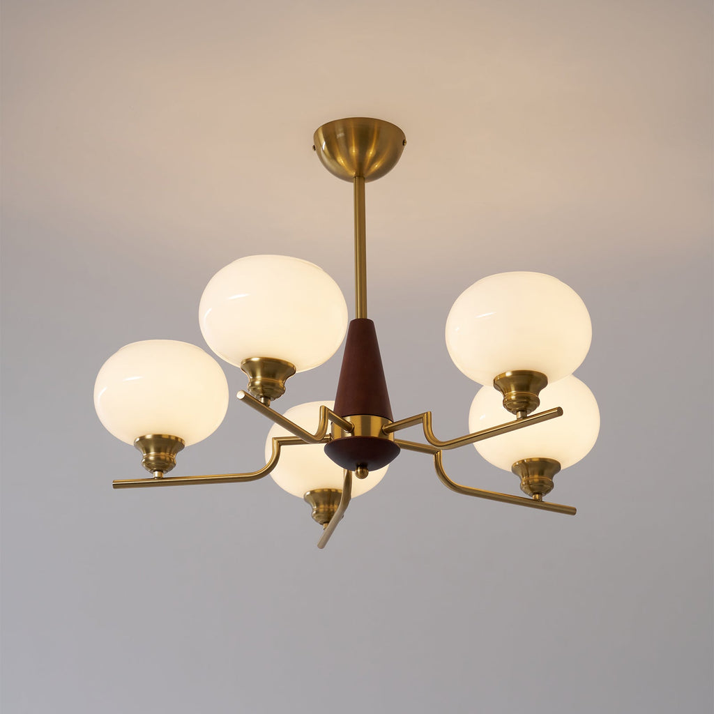The warm glow of five milky globes lights up this Clérachic chandelier, shown against a soft grey wall.
