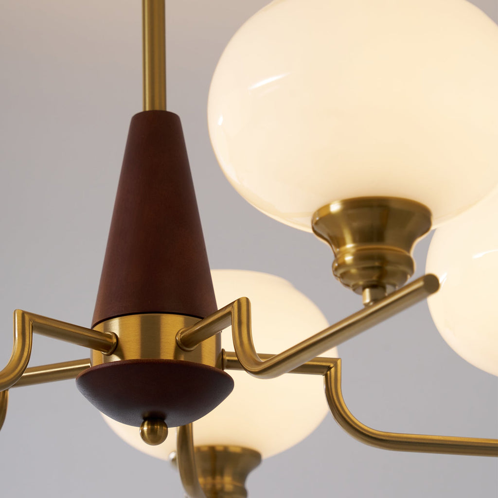 Close view of the walnut cone, brass collar and angled brass arms of this Clérachic chandelier, with a large milky globe above.
