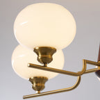 Close view of a brass lamp holder and a bent brass arm on this Clérachic chandelier, below a smooth, softly lit white globe.