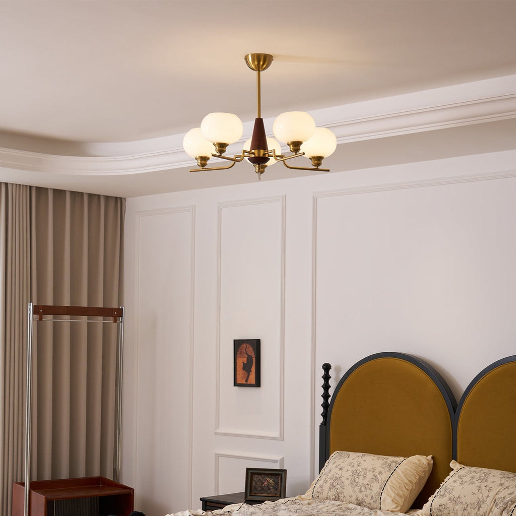 A Clérachic chandelier hangs from a coved ceiling in a bedroom with white wall panels and a mustard arched headboard.