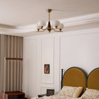 This Clérachic chandelier hangs in a pale room with white wall panels, above a bed with a mustard headboard and floral linen.