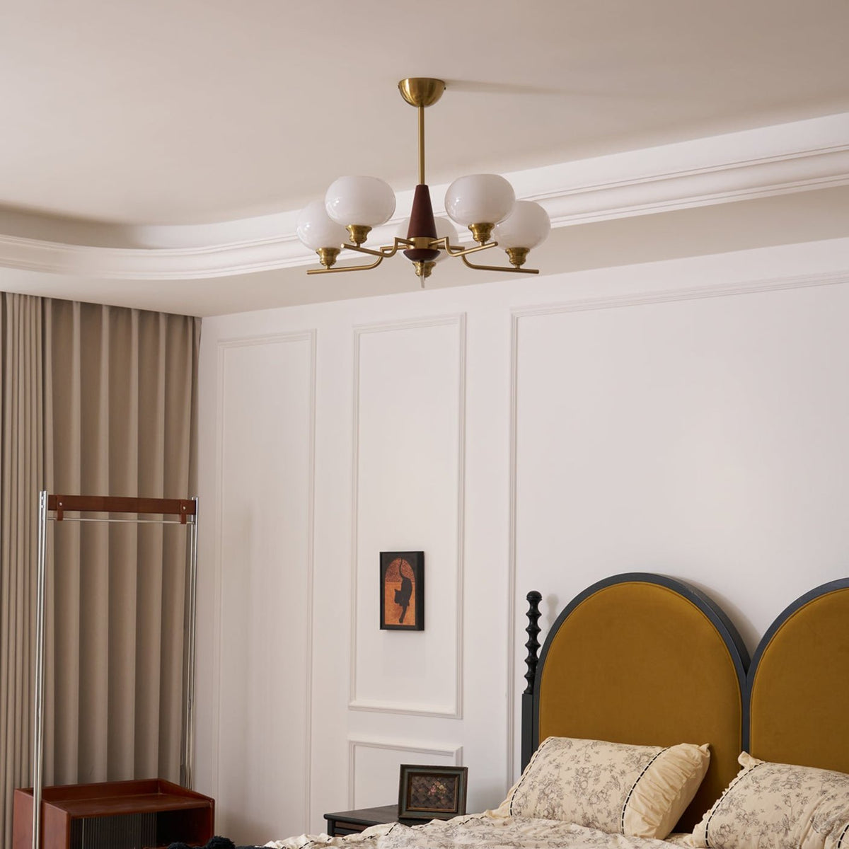 This Clérachic chandelier hangs in a pale room with white wall panels, above a bed with a mustard headboard and floral linen.