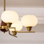 Close view of the brass fittings, bent arms and softly lit white globes on this Clérachic chandelier, against a pale wall.
