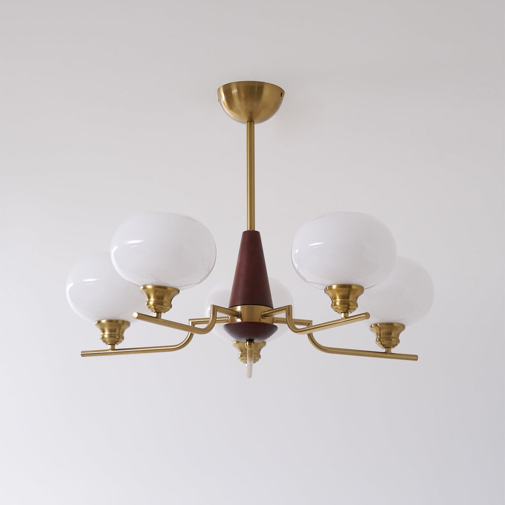 This Clérachic chandelier has five white glass globes on bent brass arms around a walnut cone, on a pale wall.