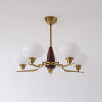 This Clérachic chandelier has five white glass globes on bent brass arms around a walnut cone, on a pale wall.