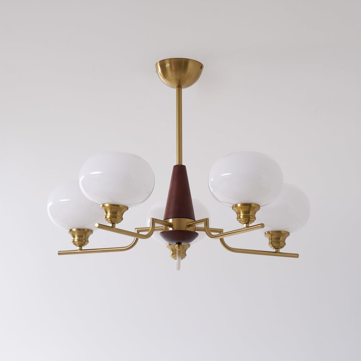 This Clérachic chandelier has five white glass globes on bent brass arms around a walnut cone, on a pale wall.