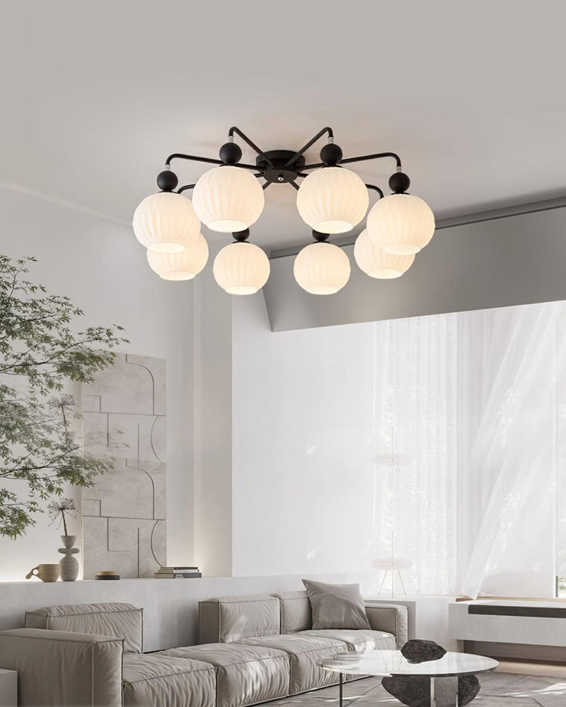 Black-armed Clérachic ceiling light with eight frosted globes, in a pale living room with a grey sofa and a tall indoor tree.